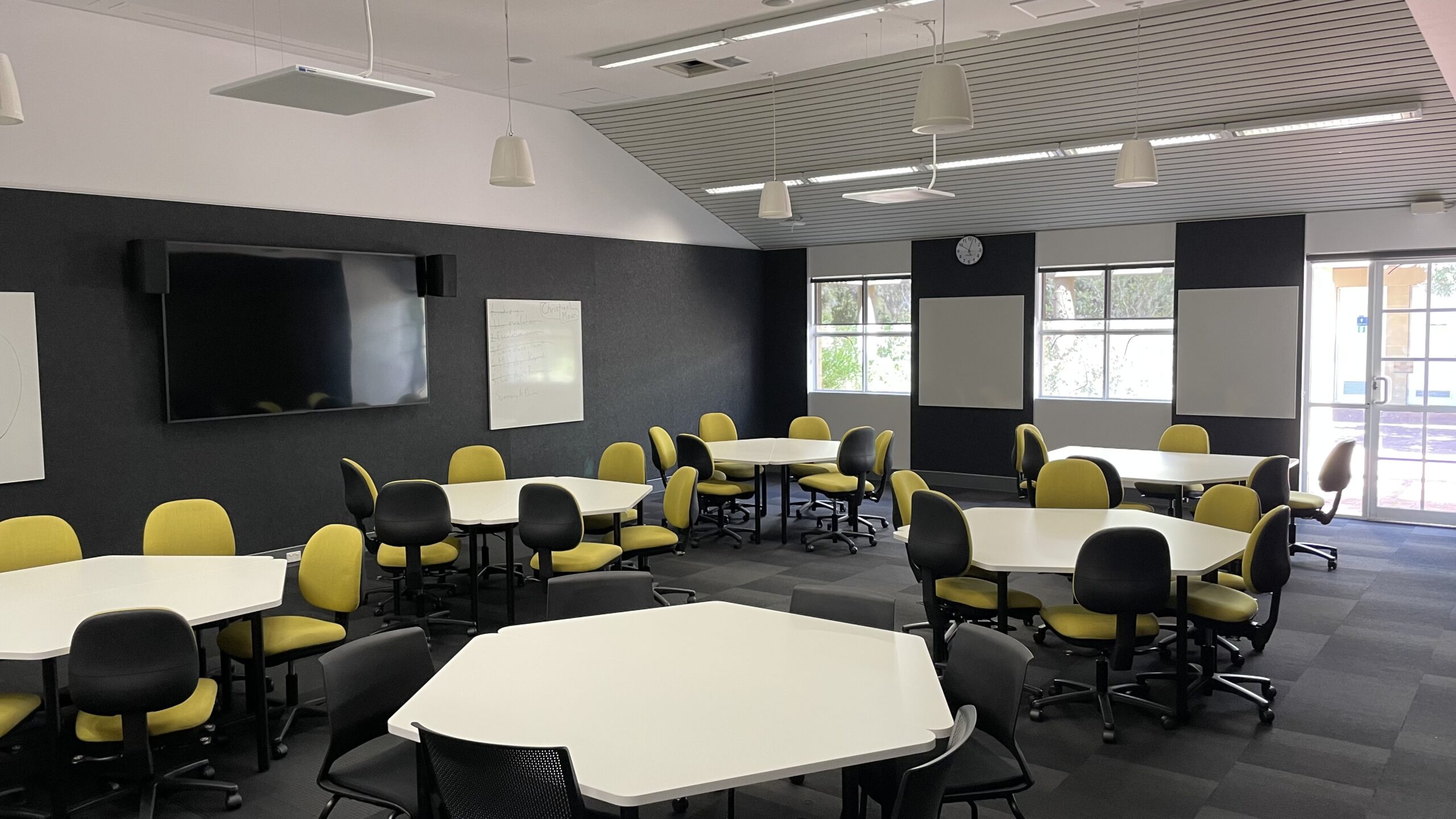 ECU's pilot learning classrooms, featuring tables, chairs, whiteboards, and new technology such as overhead microphones and speakers. The tables are designed for agile rearranging of furniture for flexibility, adaptability, and active learning.